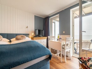 A bedroom with a bed, a desk, and a chair. There is a television on a stand and a window with curtains. - Holiday Apartment With 1 Bedroom (Wyk auf Foehr)