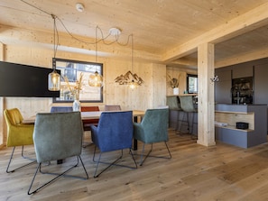 Interior moderno com teto de madeira, sala de jantar com cadeiras e mesa, e cozinha com banquetas.