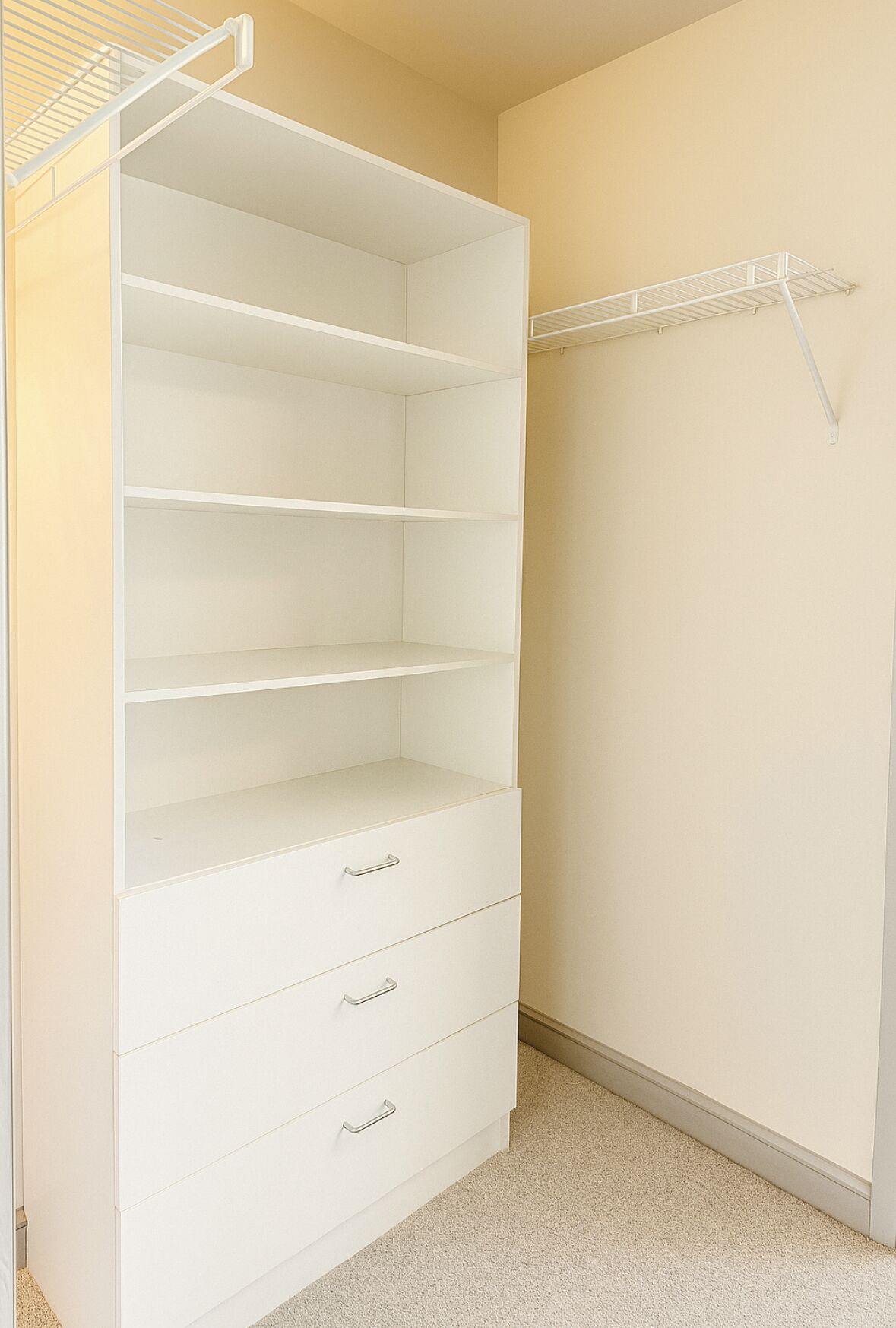 Un placard avec des étagères et des tiroirs ouverts, une tringle pour suspendre les vêtements et un sol recouvert de moquette.