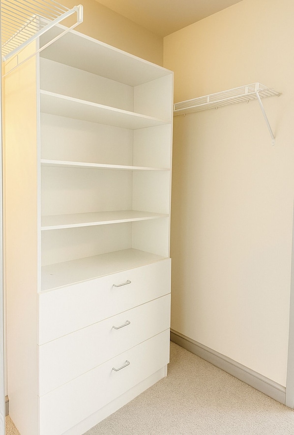 A closet with open shelves and drawers, a hanging rod, and a carpeted floor.