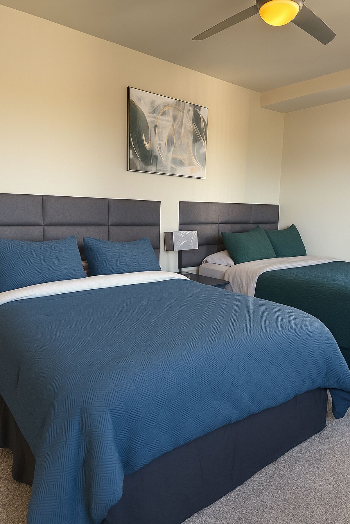 Une chambre d’hôtel avec deux lits, un ventilateur de plafond et un tableau accroché au mur.