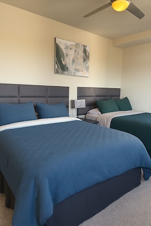 A hotel room with two beds, a ceiling fan, and a painting on the wall.