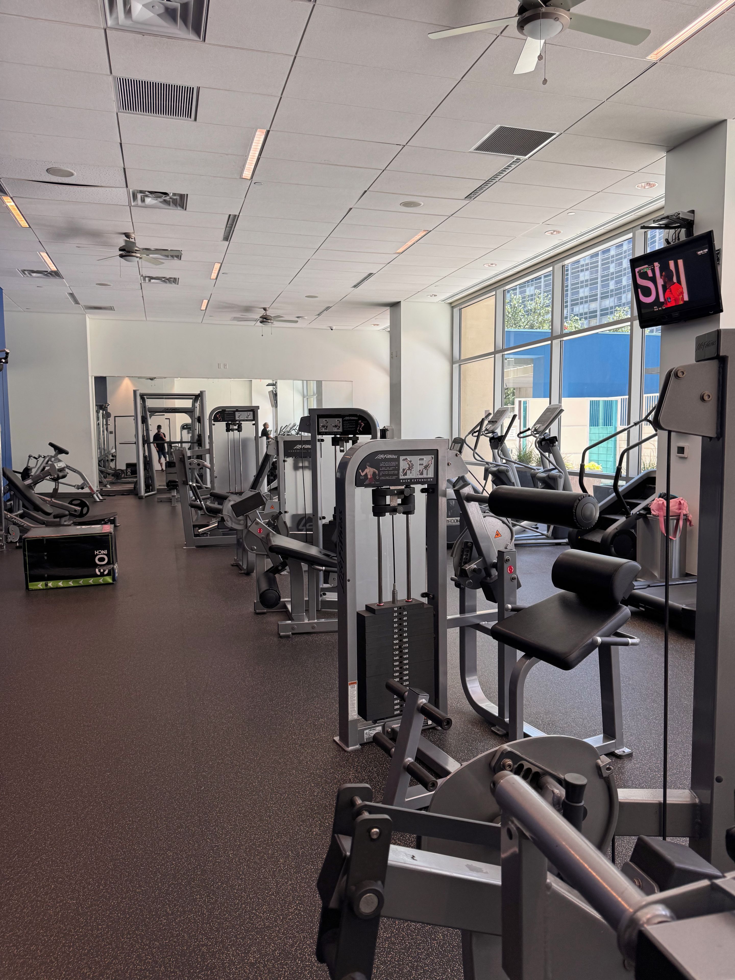 Une salle de sport équipée de divers appareils d’exercice, d’un écran de télévision et de grandes fenêtres.