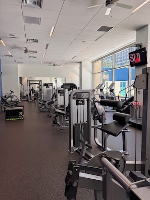 A gym with various exercise machines, a television screen, and large windows.