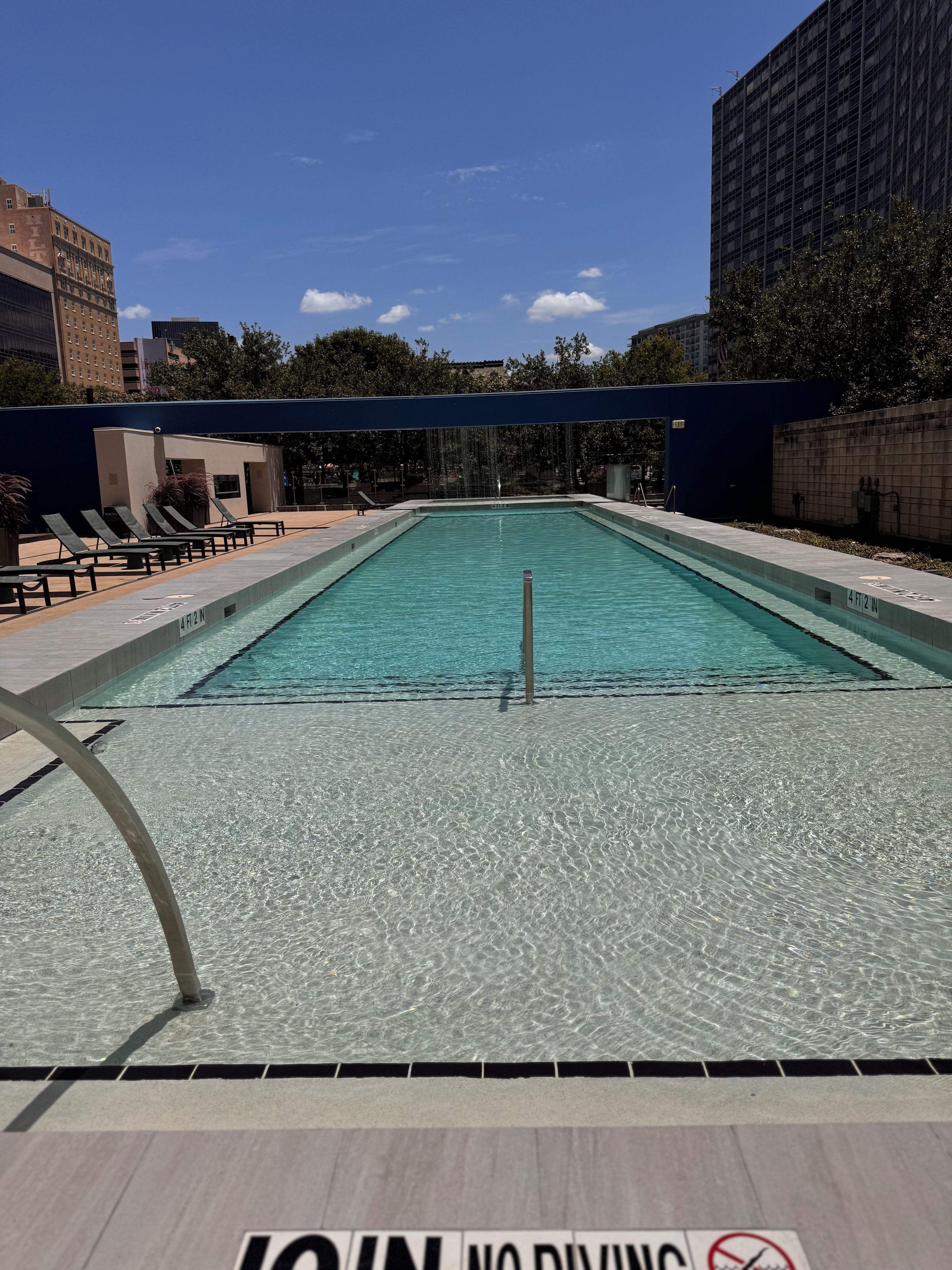 Une piscine à l’eau claire, entourée de chaises longues et agrémentée d’un panneau indiquant qu’il est interdit de plonger.