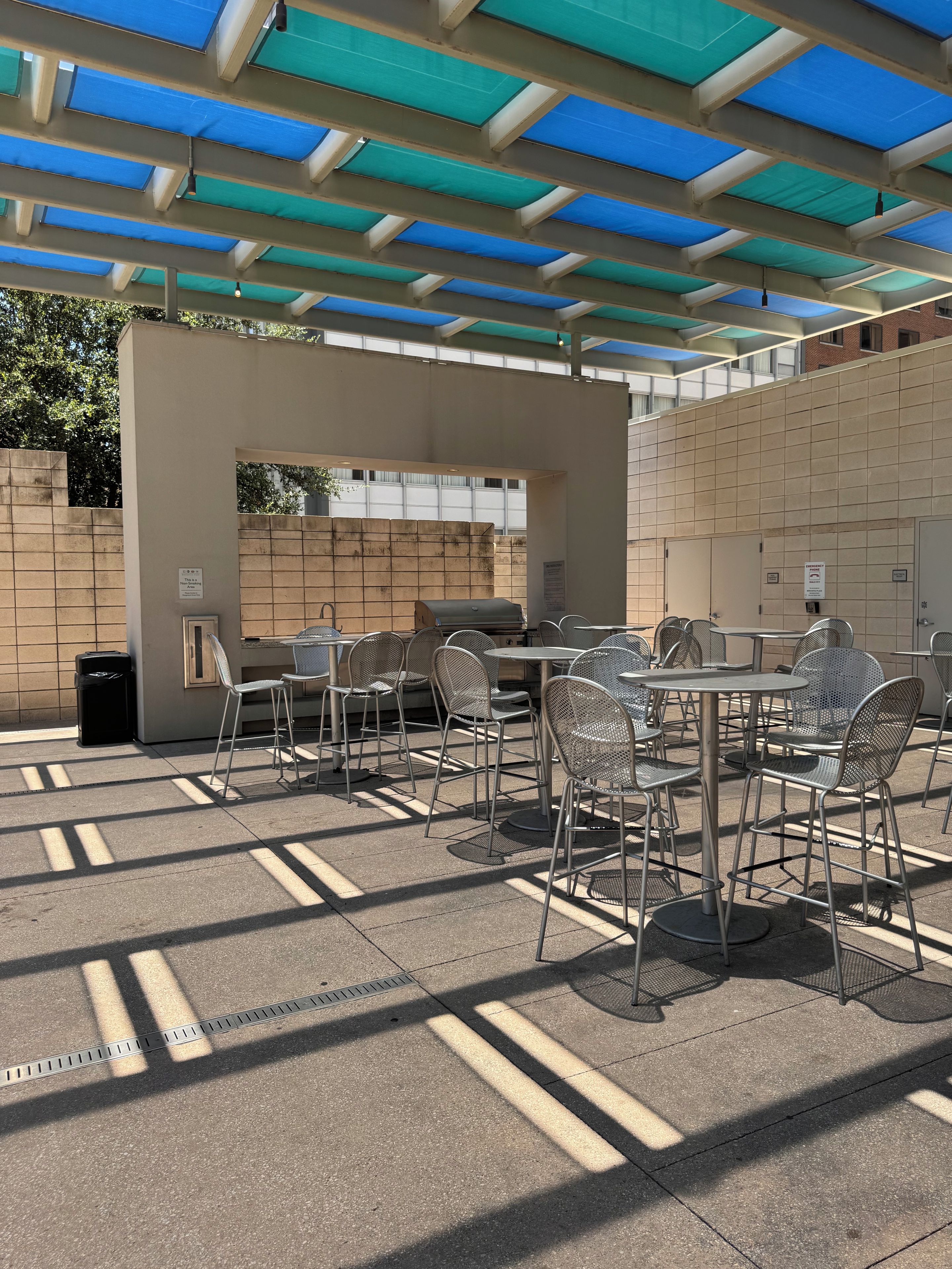 An outdoor patio with metal chairs and tables, a barbecue grill, and a covered area with a blue and green roof.