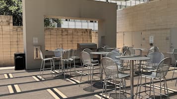 An outdoor patio with metal chairs and tables, a barbecue grill, and a covered area with a blue and green roof.
