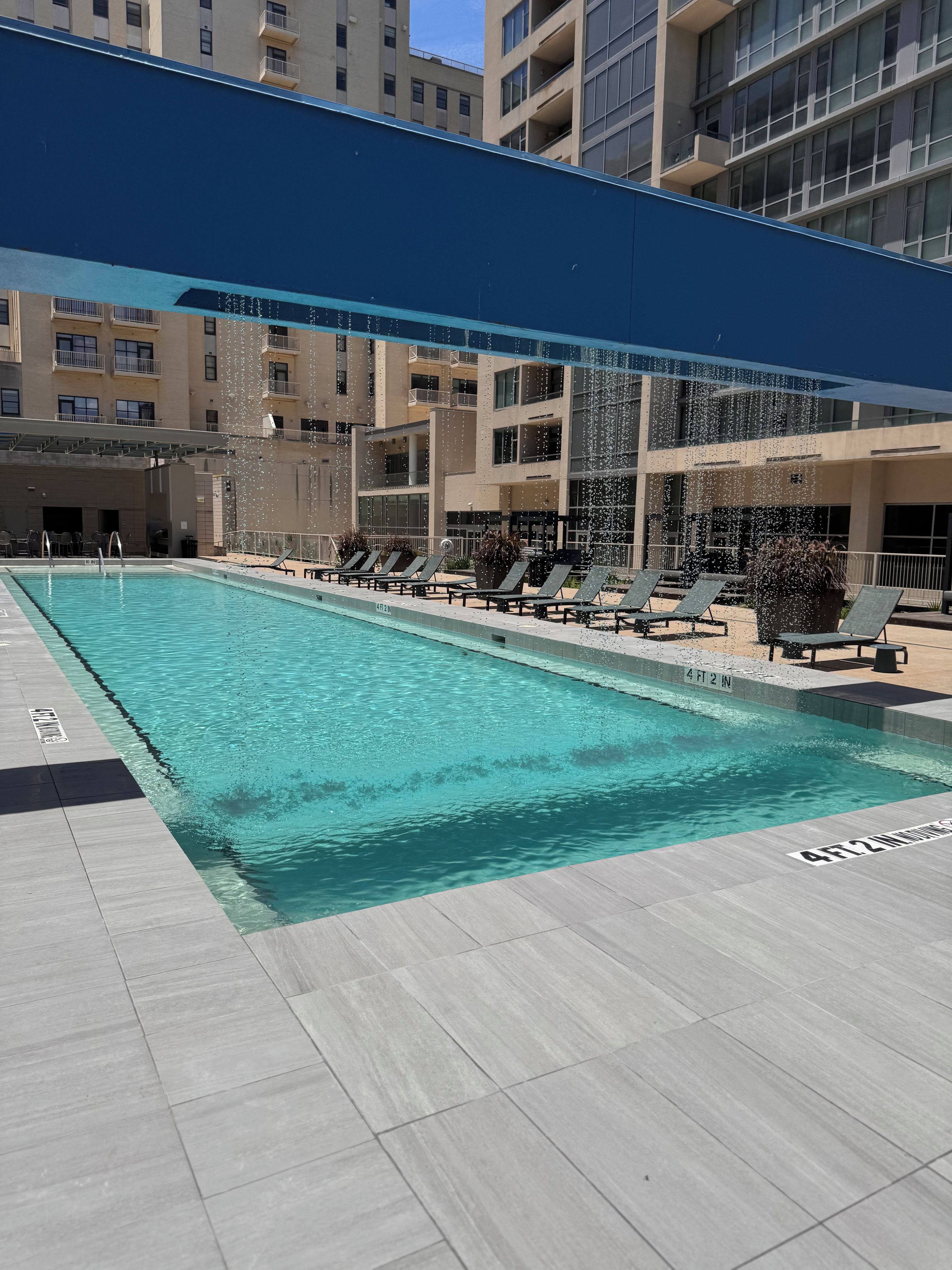A swimming pool with lounge chairs and a covered area, surrounded by multi-story buildings.