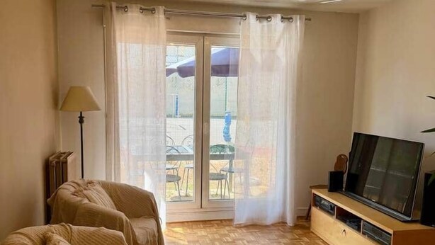 A room with a sofa set, a television on a wooden stand, and a view through a glass door to an outdoor area. - Le Chêne - Charming Apartment with a Garden (Lyon)