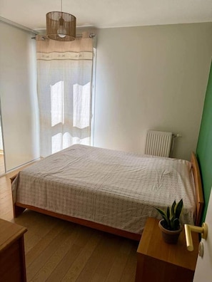 Une chambre à coucher avec un lit, un radiateur, une fenêtre avec des rideaux et une plante en pot.