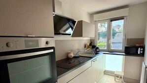 A compact kitchen with a built-in oven, a microwave, and a hanging light fixture. - Le Chêne - Charming Apartment with a Garden (Lyon)
