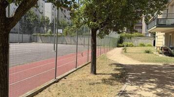 Un sendero conduce a una pista roja, rodeada por una cerca y árboles, con un edificio al fondo.