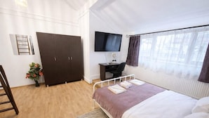 Ein Hotelzimmer mit Bett, Schreibtisch mit Stuhl, Kleiderschrank, Fernseher und einem Fenster mit Vorhängen.