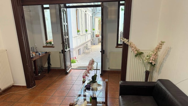 Ein Wohnzimmer mit einer schwarzen Couch, einem Glastisch mit Blumen und Blick auf einen Innenhof durch offene Türen.