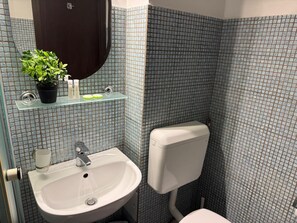 Une salle de bain avec un lavabo blanc, un miroir, des toilettes et une étagère contenant des articles de toilette.