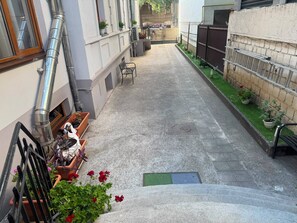 A narrow alleyway with a bench, potted plants, and a metal fence.