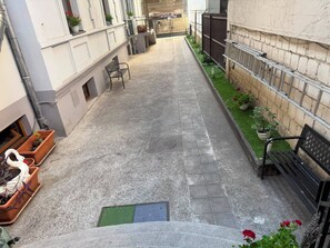 Un patio estrecho con un sendero empedrado, bancos, plantas en macetas y un pequeño jardín.