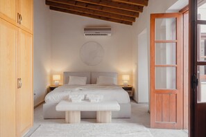 A bedroom with a bed, bedside lamps, a round wall decoration, and a wooden door. - The Bakery - A Luxury Village Stone House with Pool. Pet Friendly! (Kalavasos)