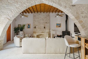 Une pièce chaleureuse avec un mur en pierre, une cheminée, un ventilateur de plafond et un plafond en bois rustique.