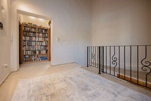 Un escalier recouvert de moquette, doté d’une rampe en métal, mène à une pièce où se trouve une bibliothèque.