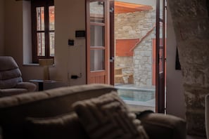 Ein Wohnzimmer mit einer Couch, einem Tisch und Blick auf einen Außenbereich mit Pool und Steinmauern.