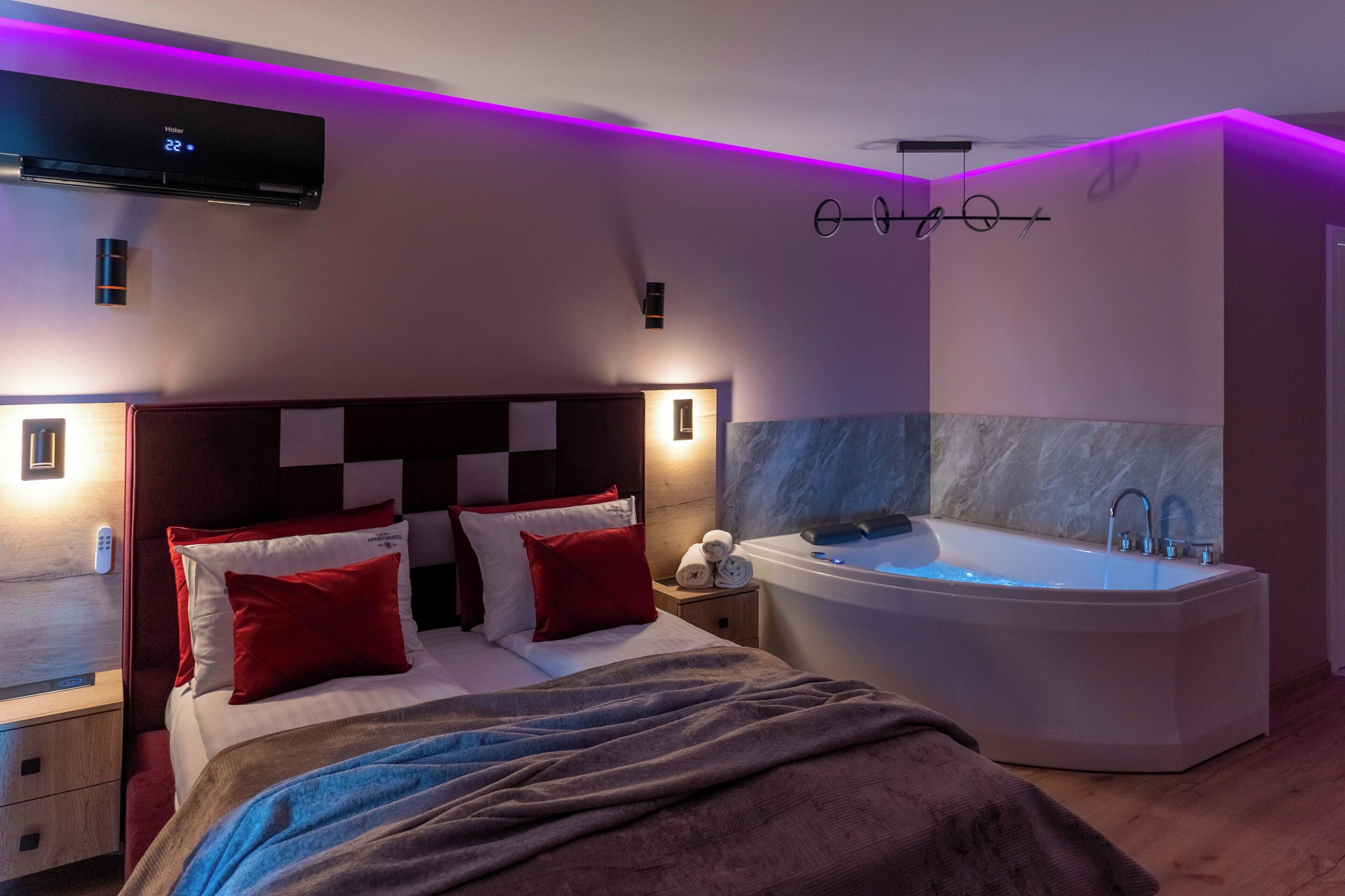 A modern bedroom with a large bed, a built-in bathtub, and a wall-mounted air conditioning unit.