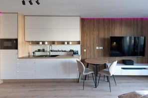 Una cuina moderna amb armaris blancs, una illa central i una zona de dinar amb dues cadires.