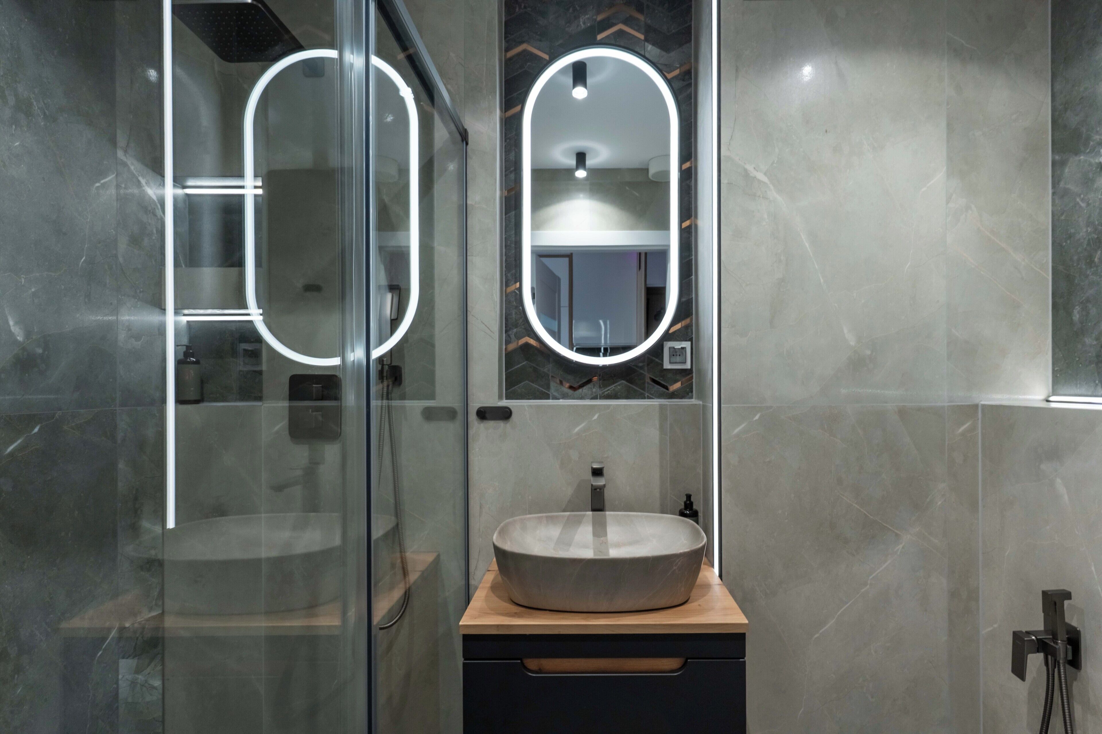 Ein modernes Badezimmer mit Duschkabine aus Glas, einem runden Spiegel mit Beleuchtung und einem Aufsatzwaschbecken auf einer Holzablage.