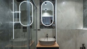 A modern bathroom with a glass shower enclosure, a round mirror with a light, and a vessel sink on a wooden countertop. - Portovo Private Jacuzzi & AC Suite (Gdańsk)