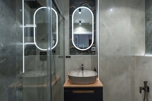 A modern bathroom with a glass shower enclosure, a round mirror with a light, and a vessel sink on a wooden countertop. - Portovo Private Jacuzzi & AC Suite (Gdańsk)