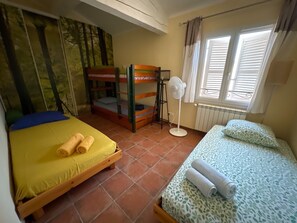 A room with two beds, a standing fan, and a window with blinds. - Maison chaleureuse de 5 chambres située en Provence idéale pour les familles (Brue-Auriac)
