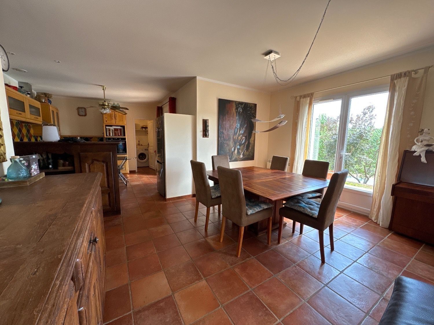 A spacious kitchen with a dining area, a large window, and a painting on the wall.