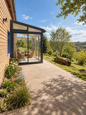 Ein modernes Haus mit einer gläsernen Veranda, Gartenmöbeln und einem angelegten Garten.