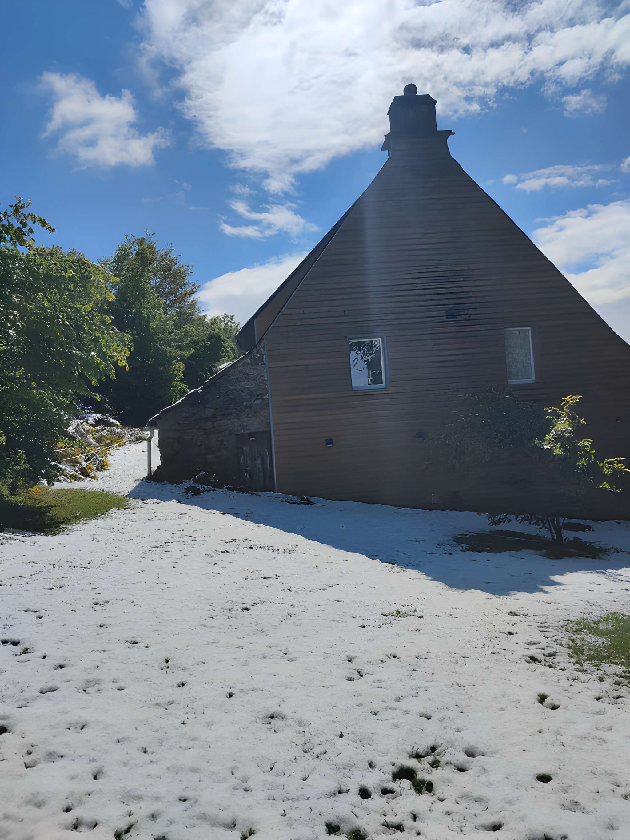 A wooden building with a gabled roof, a small window, and a stone wall to the left.