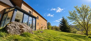 Ein modernes Haus mit großen Glasfenstern, einer Holzfassade und einem Rasenstück mit einem Felsen und Bäumen.