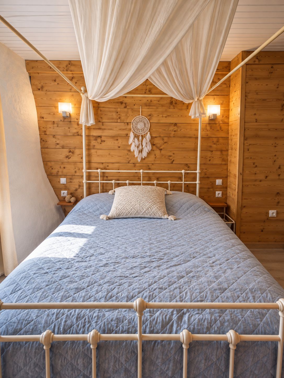 A bed with a white metal frame, a blue quilted bedspread, and a white canopy.