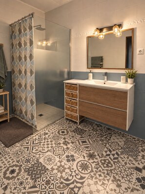 Un baño con ducha, un lavabo con espejo y baldosas de suelo estampadas.