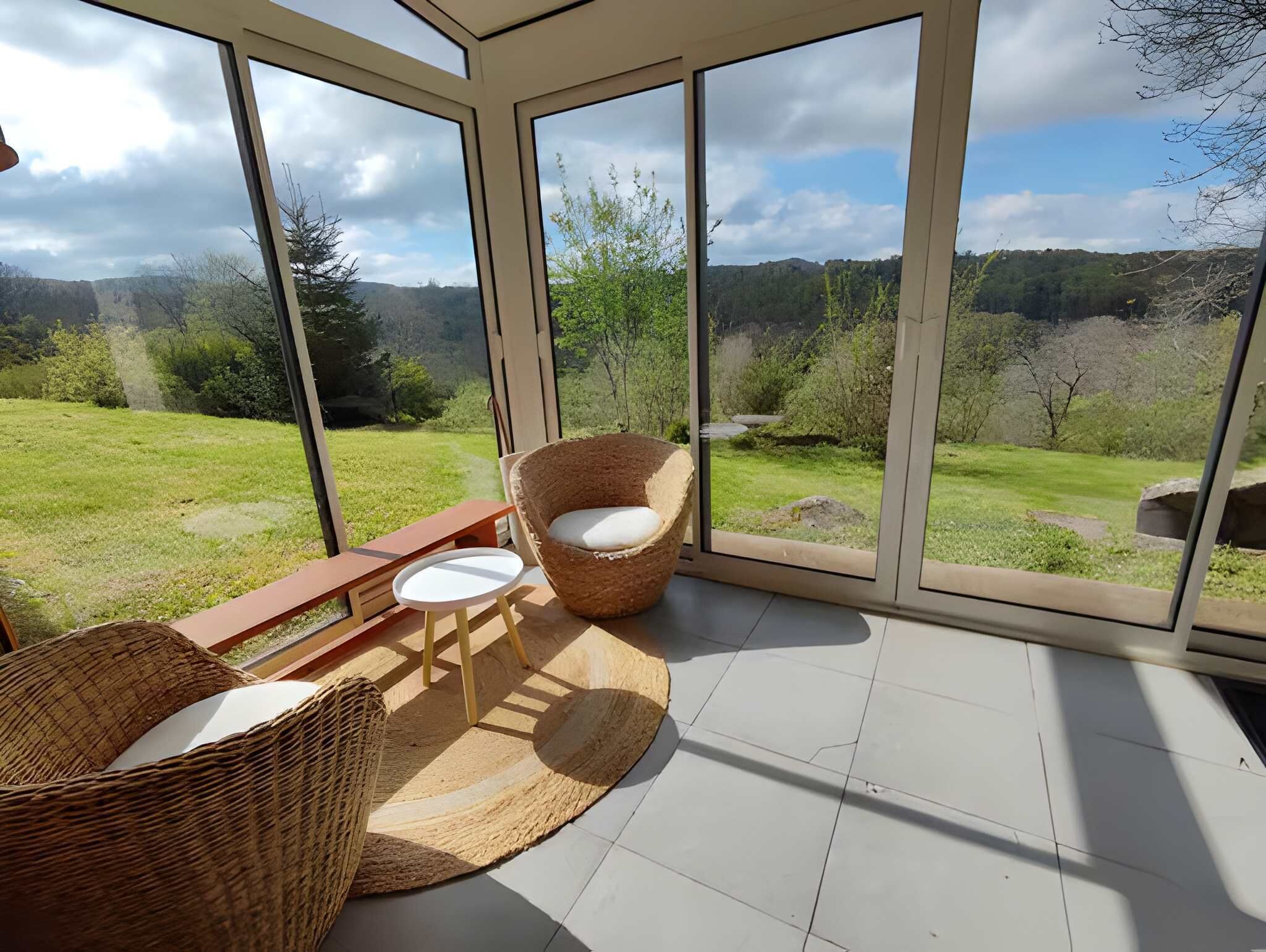 A sunroom with large windows, wicker furniture, and a view of a grassy landscape.