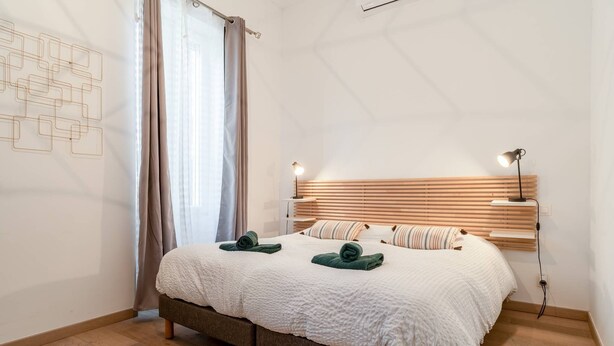 A bedroom with a bed, wooden headboard, bedside lamps, and a window with curtains. - Holiday Home 'Le Mas De KItty' with Private Pool, Wi-Fi and Air Conditioning (Saint-Rémy-de-Provence)
