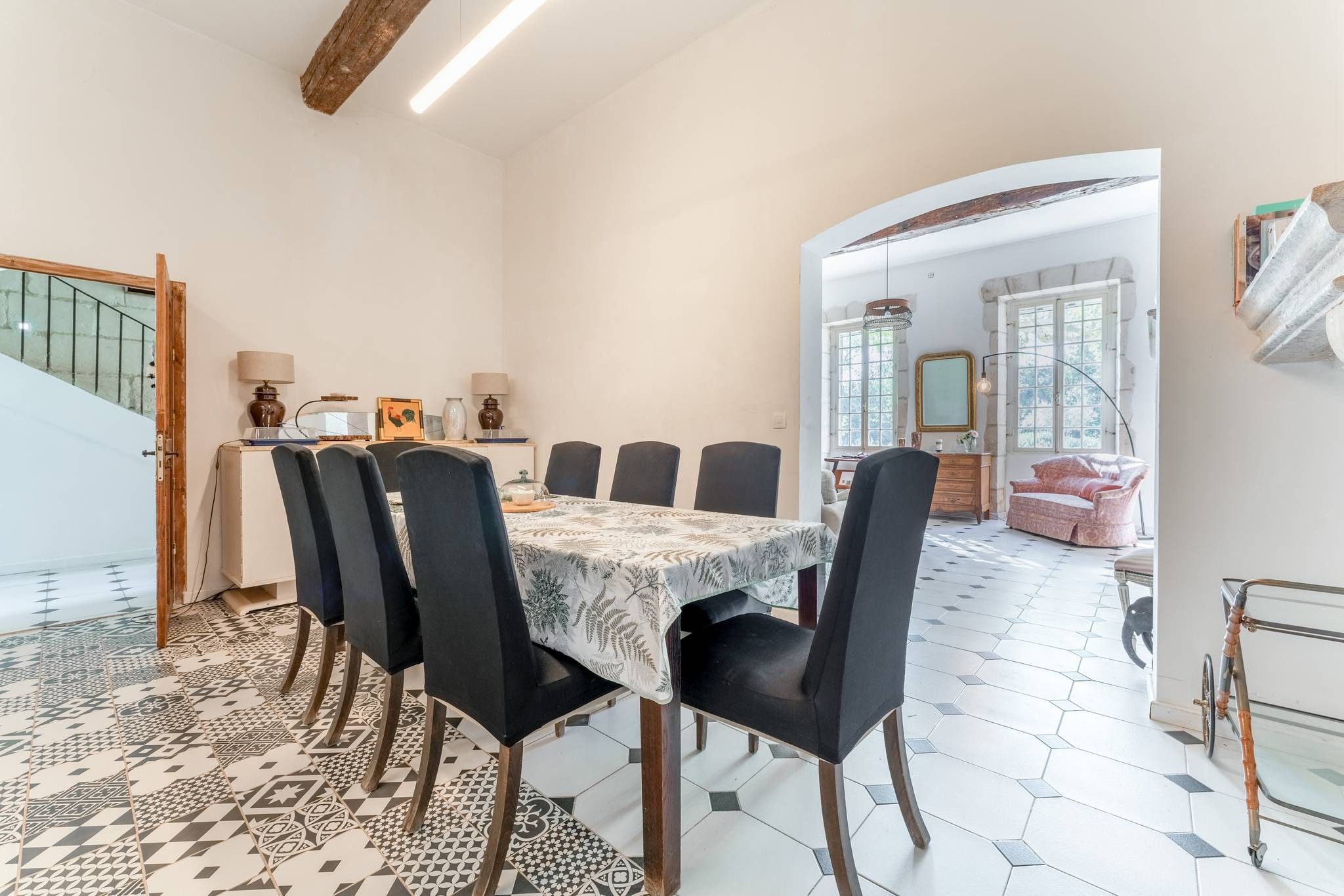 Un coin repas avec une table dressée pour six personnes, entourée de chaises, dans une pièce dotée d’un escalier et offrant une vue sur l’extérieur.