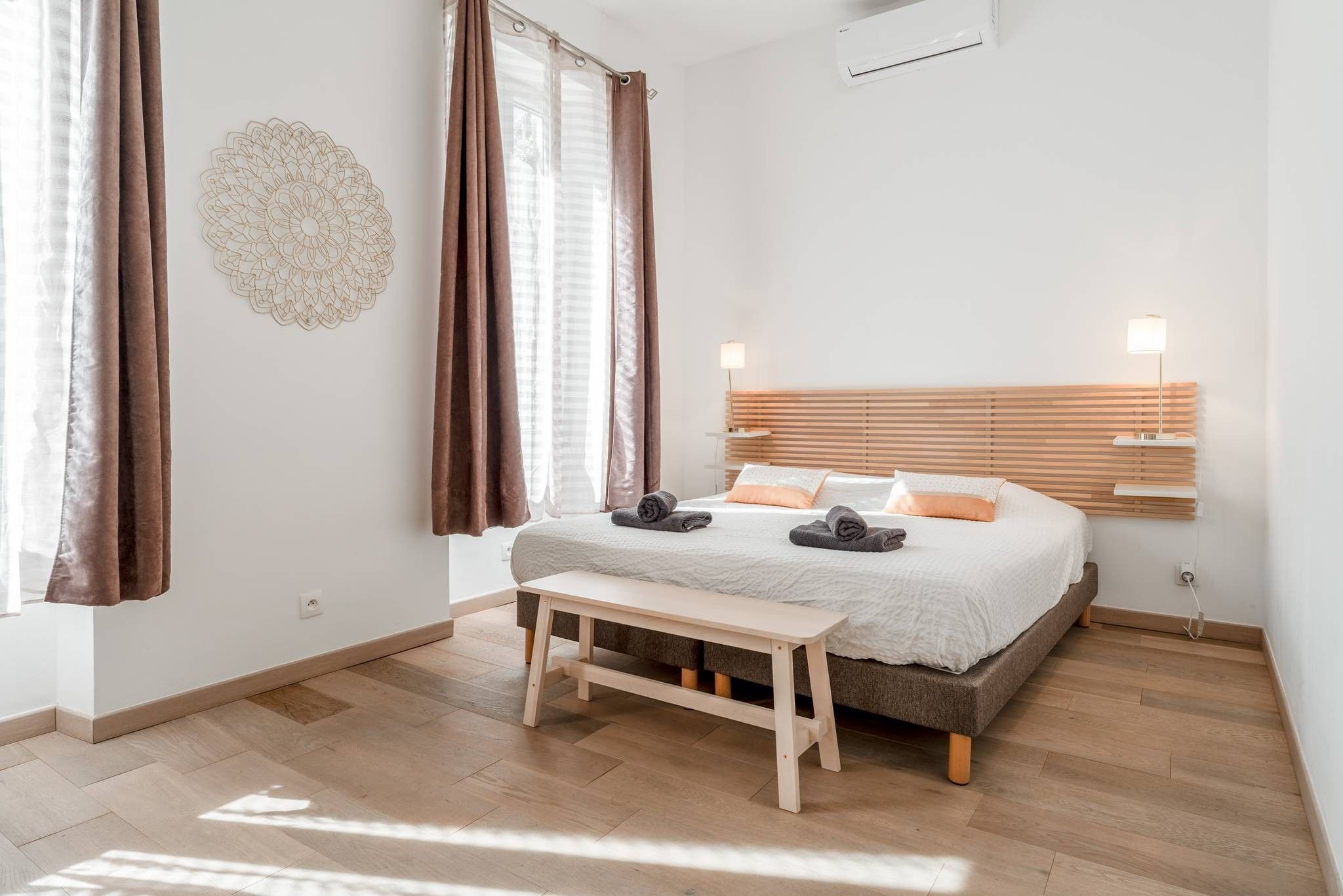 A bedroom with a bed, bedside lamps, a bench, and a wall decoration.