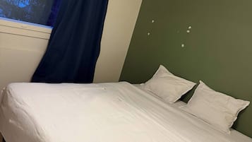 A bed with white bedding, a window with blue curtains, and a green wall.