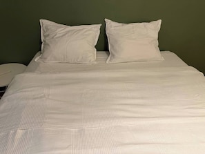 A bed with white bedding and pillows, a white bedside table, and a green wall.