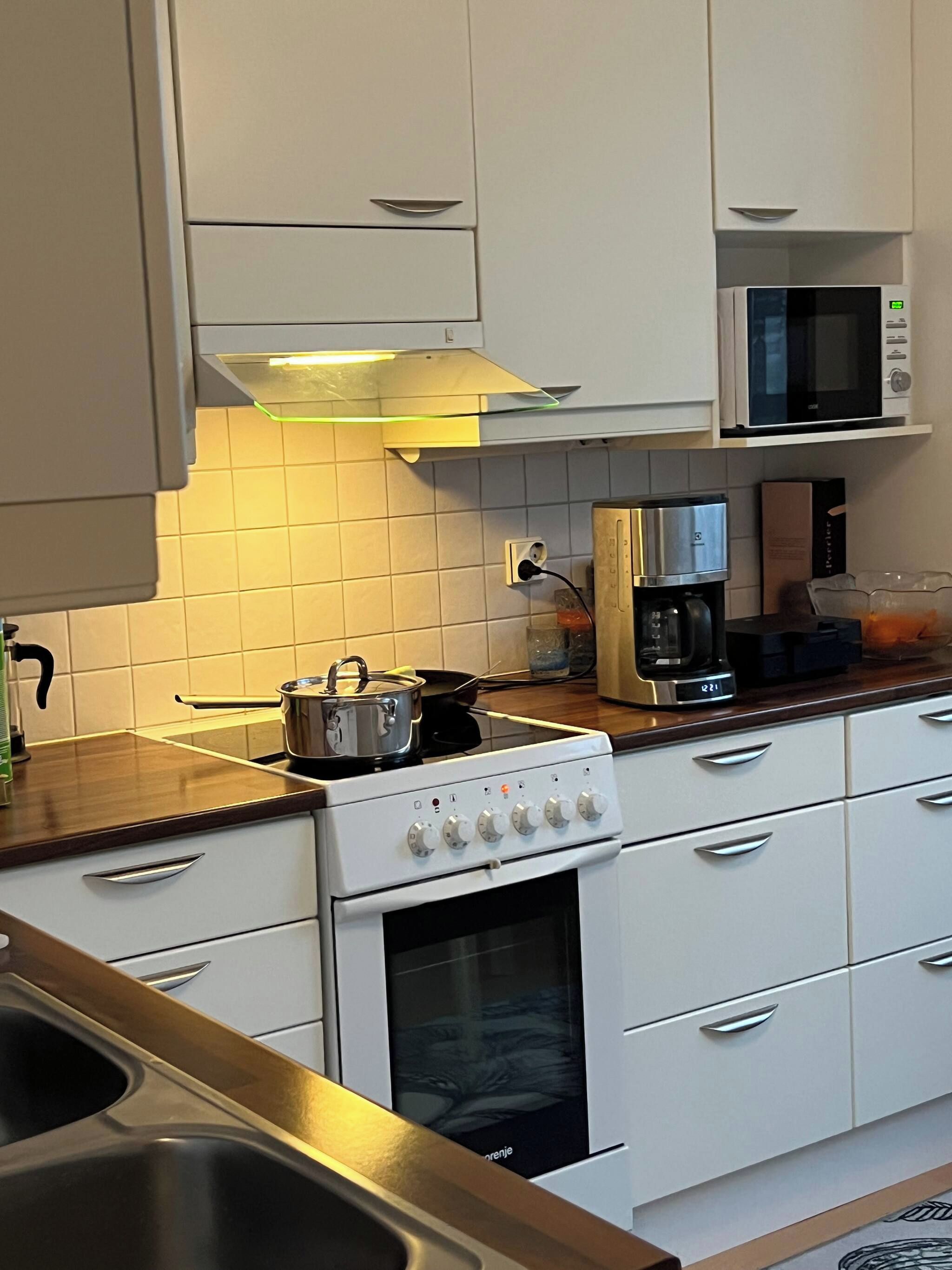 A kitchen with white cabinets, a stove, a microwave, and a coffee maker.