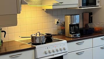 A kitchen with white cabinets, a stove, a microwave, and a coffee maker.