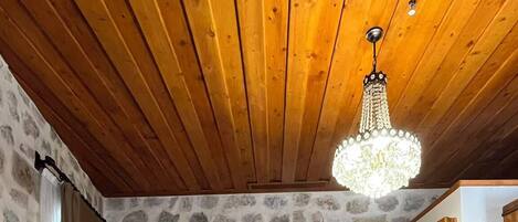 A bedroom with a wooden ceiling, stone walls, a bed with white bedding, a patterned floor, and a chandelier.