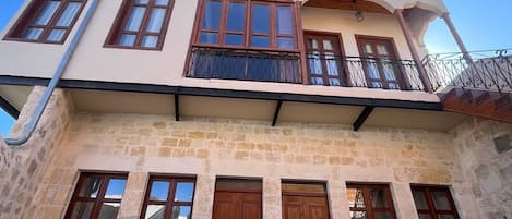 Un edificio de dos pisos con balcón, fachada de piedra y múltiples ventanas.