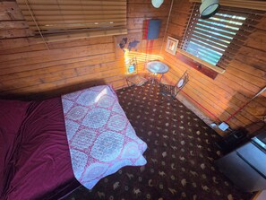 A room with a bed, a small table with chairs, a world map on the wall, and a window with blinds.