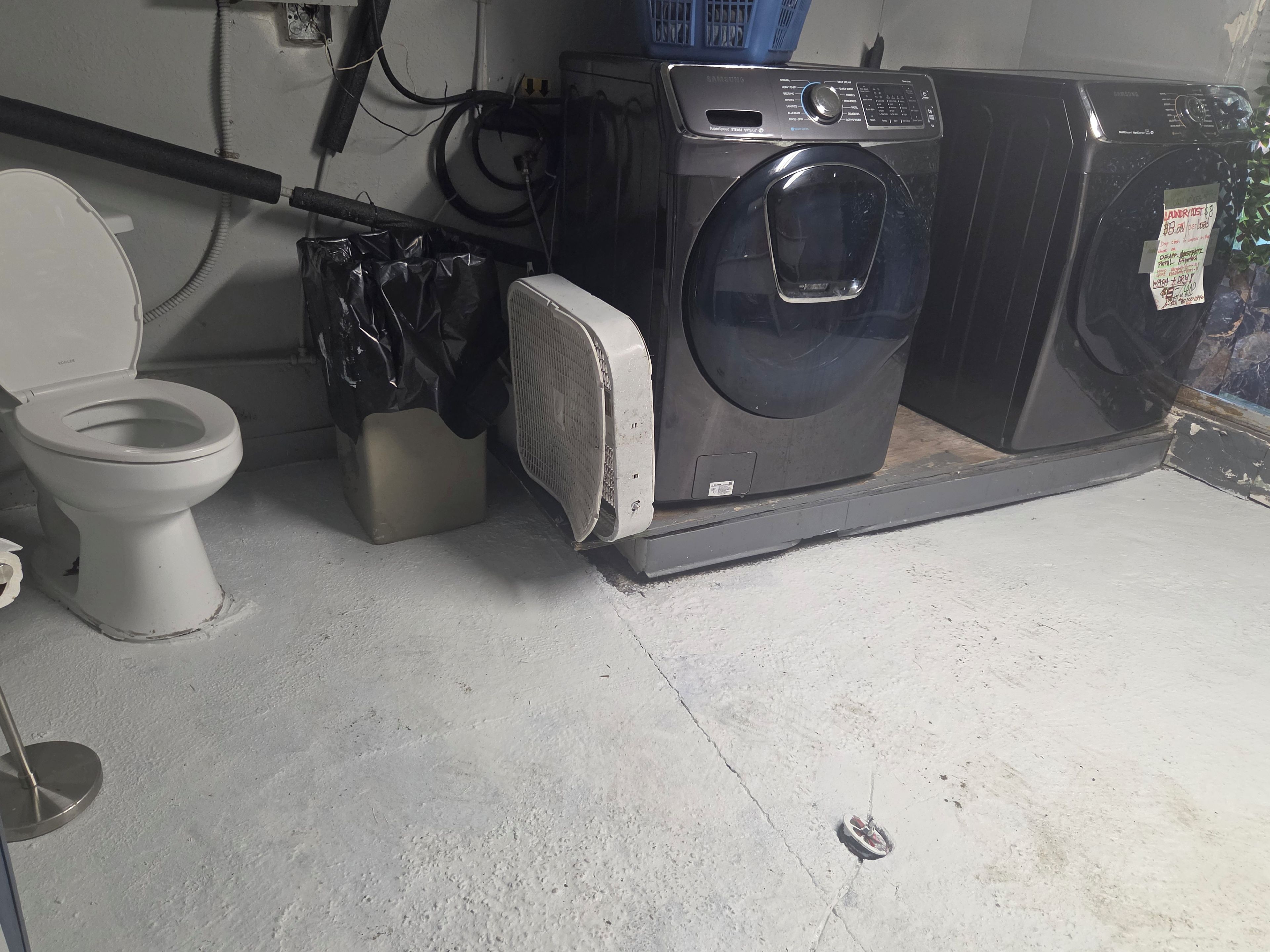 A compact bathroom with a toilet, washing machine, and a small trash bin.
