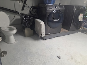 A compact bathroom with a toilet, washing machine, and a small trash bin.
